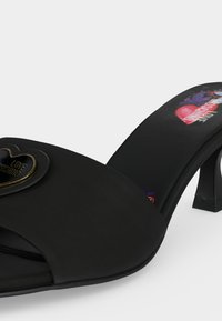 Μαύρο mule σανδάλι με ψηλό τακούνι, ανοιχτά δάχτυλα, καρδιά με το έμβλημα "Love Moschino" και πολύχρωμο σχέδιο λογότυπου στην εσωτερική σόλα.