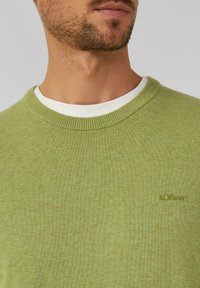 Grüner Rundhalsausschnitt-Pullover aus weichem Strickmaterial. Verfügt über einen weißen Innenkragen und ein kleines s.Oliver-Logo auf der Vorderseite.