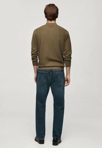 Oliivinvihreä neulepaita ja tummansiniset farkut. Neulepaidassa on pyöreä kaula-aukko ja resorikäänteet, kun taas farkuissa on kaksi takataskua.