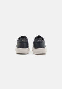 Navy leather shoes with a white rubber sole. Features minimalistic design and subtle branding details in gold, black, and white on the heel.