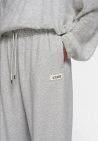 Lyse grå sweatpants lavet af blødt stof, med elastisk talje og snor, sidelommer og et vævet mærke.