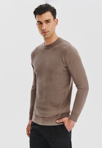 Brązowy sweter o teksturowym wzorze, z okrągłym dekoltem, długimi rękawami i ribbowanym wykończeniem. W połączeniu z ciemnymi spodniami, minimalistyczny design.