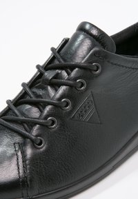 Svarta läderskor med snörning, rund metallöglor och präglad ECCO-logotyp på sidan, visade mot en vit bakgrund.