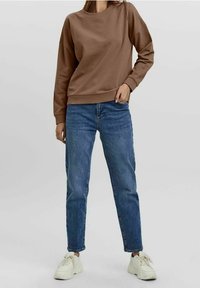 Hnědá mikina s kulatým výstřihem, žebrovanými manžetami a lemem. Kombinováno s klasickými modrými džínami a bílými teniskami. Ležérní vzhled.