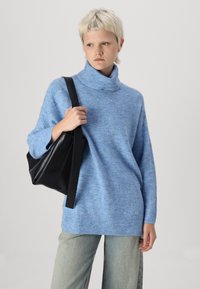 Svijetloplavi turtleneck pulover od pletene tkanine s opuštenim krojem. Uparen s izblijedjelim širokim trapericama i crnom kožnom torbom preko ramena.