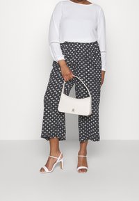 Witte lange mouwen top, gestreepte zwart-witte cropped broek, witte gespsandaaltjes en een witte handtas met gouden hardware.