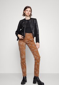 Casaco de couro preto com detalhes canelados, combinado com calças em padrão de pele de cobra castanha. A modelo usa botas pretas de salto chunky.