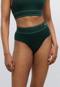 Σκούρο πράσινο ριμπ βαμβακερό μπουστάκι και σετ σλιπ ψηλόμεσο με λαστιχένιες ταινίες με το λογότυπο και διακριτικές λεπτομέρειες με αντίθετη ραφή.