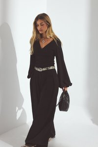 Črna majica z dolgimi rokavi in v-izrezom, hlače širokega kroja visoko pasu ter pas z vzorcem kačje kože. Drži črno tkanino torbico.