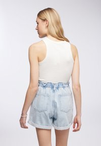 Top in cotone bianco a coste abbinato a pantaloni shorts in denim azzurro chiaro con vita alta, fascia elastica e orlo risvoltato. Tasche posteriori visibili.