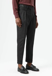 Grijze plissé broek met een riem voorzien van een rechthoekige gesp, gecombineerd met zwarte loafers. Gladde stof, taps toelopende pasvorm en omslagzoom.