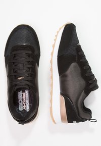 Schwarze Sneakers aus strukturiertem Mesh und synthetischen Materialien, mit einer weißen Zwischensohle und einer hellbraunen Gummisohle. Schnürdesign.