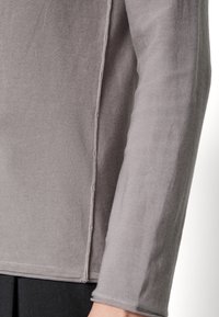 Szara koszula z długim rękawem o fakturowanej tkaninie, widocznych szwach i luźnym kroju. Posiada okrągły dekolt i prosty dół.