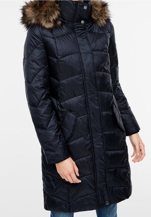 Manteau d'hiver long noir matelassé avec capuche bordée de fourrure, boutons-pression à l'avant et poches latérales, porté par une personne les mains détendues le long du corps.