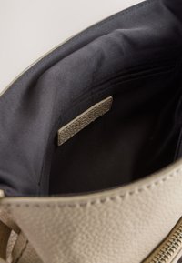 Interiorul genții din piele bej deschis cu căptușeală din țesătură neagră, având o etichetă texturată din piele și o închidere cu fermoar de-a lungul marginii.