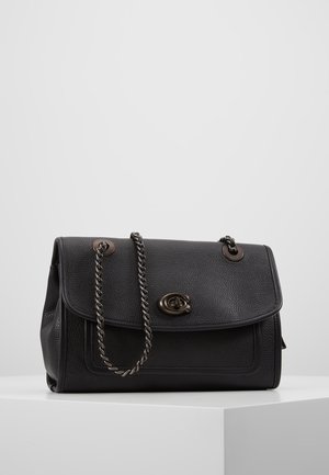 Zwarte leren handtas met een voorflap, metalen draaivergrendeling en een donker metalen ketting schouderriem, rustend op een wit oppervlak.