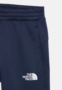 Jūras tumši zili sporta bikses ar gludu tekstūru, elastīgu jostu, sānu kabatām un baltu "The North Face" logotipu uz augšstilba.
