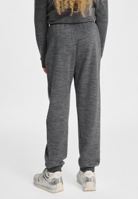 Grau gestrickte Jogginghosen mit lockerer Passform, elastischem Bund und gerippten Säumen, kombiniert mit silbernen Sportschuhen.