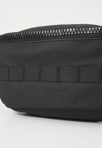 Marsupio nero con finitura liscia opaca, dotato di chiusura con cerniera superiore e spallaccio in tessuto testurizzato. "LYLE & SCOTT" impresso sul lato.