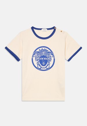 Chemise crème à manches courtes avec bordure bleue et logo tête de Méduse bleu sur le devant, avec deux petits boutons dorés sur l'épaule.