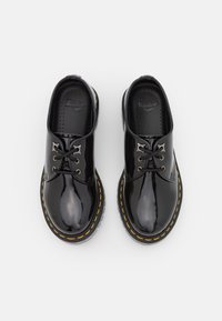 Czarne lakierowane buty ze skórzaną podeszwą, zaokrąglonym noskiem, płaską podeszwą, żółtym przeszyciem i czarnymi sznurówkami. Prosty design z połyskującym wykończeniem.