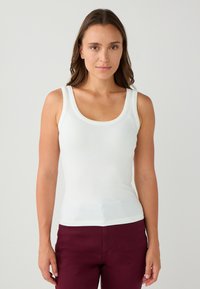 Weißes geripptes Tanktop mit breiten Trägern und Rundhalsausschnitt, kombiniert mit burgunderfarbenen Hosen. Glatte Textur und figurbetontes Design.