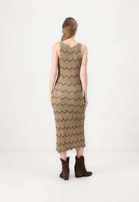 Abito in maglia con motivo a zigzag in tonalità terrose. Caratterizzato da una forma aderente e orlo a ginocchio. Abbinato a stivali alla caviglia marroni.