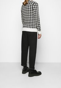 Suéter con patrón de espiga en blanco y negro, textura de punto, con borde acanalado blanco, combinado con pantalones negros de corte suelto y zapatos negros.