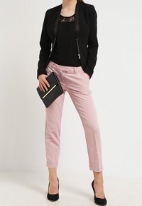 Černý blazer s saténovým lemem, krajkový top, růžové pouzdrové kalhoty a černá kabelka. Modelka má na sobě černé vysoké podpatky.