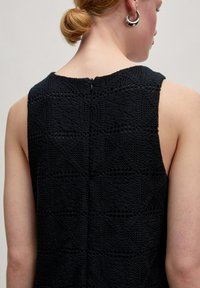 Schwarzes ärmelloses Kleid mit strukturiertem Strickmuster, rundem Ausschnitt und Reißverschluss auf der Rückseite. Schlichtes, minimalistisches Design.