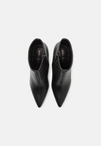 Botines de cuero negro hasta el tobillo con puntera afilada, que presentan cremalleras laterales y una textura suave. El interior tiene letras doradas que dicen "ANNA FIELD."