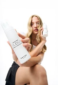 Witte conditionerflessen met een minimalistisch ontwerp, gelabeld "CLOUD", met zilveren tekst. Eén fles wordt prominent op de voorgrond vastgehouden.