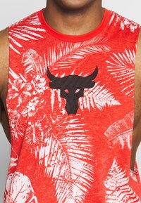 Maglietta rossa senza maniche con motivi floreali bianchi e foglie di palma, con un logo di un toro nero al centro. Tessuto misto cotone, vestibilità comoda.