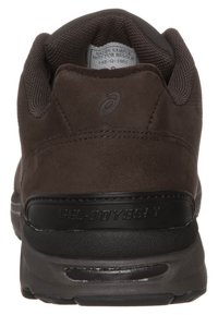 Scarpa sportiva in suede marrone con tacco arrotondato, collo in mesh testurizzato e un accento di branding nero. Presenta una suola liscia e una soletta imbottita.