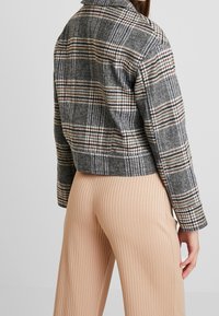 Szara kurtka w kratkę o skróconym kroju, z poziomymi i pionowymi liniami w odcieniach brązu i niebieskiego, z klasycznym kołnierzem i teksturowanym materiałem.