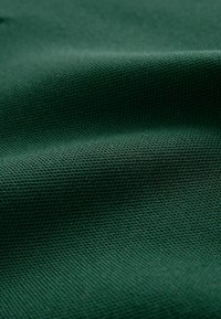 Tissu vert texturé avec un tissage serré, présentant un motif subtil et une surface lisse, adapté à diverses applications textiles.