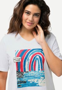 Witte t-shirt met een V-hals, voorzien van een kleurrafisch ontwerp van bogen in rood, blauw en wit, met een label "FOLLOW THE SUN". Zachte textuur.