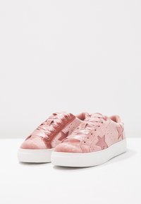 Rosa sammetssneakers med slät yta, med stjärndetaljer, satin-snören och en vit gummisula. Designen inkluderar perforerade sidor.