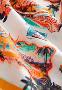 Tessuto colorato con una stampa tropicale che include conchiglie, palme e una scena di spiaggia. Il colore di base è bianco con accenti vivaci.