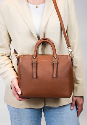 Sac à main en cuir brun avec deux poignées supérieures, fermeture éclair, bandoulière ajustable et logo embossé discret. Présente une texture lisse.