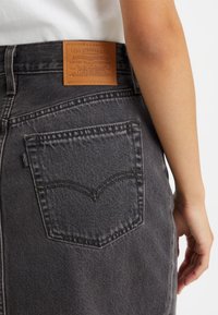 Tummanharmaat farkut, joissa on näkyvä nahkainen merkki, jossa lukee "Levi Strauss & Co.", sekä klassinen taskusuunnittelu kaarrettuine ompeleet.