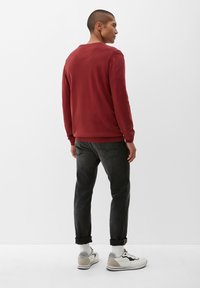 Rode sweatshirt met geribbelde manchetten en zoom, gecombineerd met donkergrijze jeans en witte sneakers met beige accenten en omgeslagen manchetten.