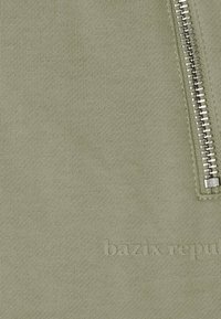 Olive green zippered sweatshirt in soft fabric with a textured finish and embossed logo "bazik republic" near the base.