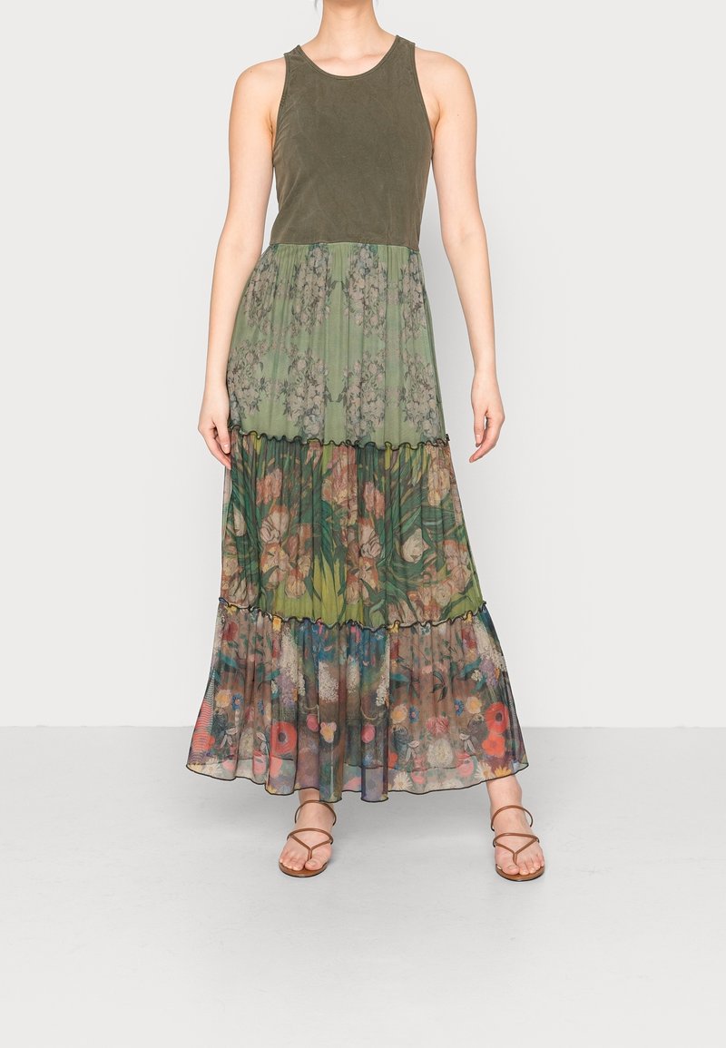Haut sans manches vert olive avec une jupe longue fluide à volants et imprimé floral dans des tons verts, roses et bruns, assorti à des sandales marron à lanières.