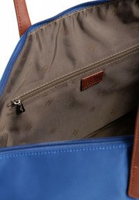 Borsa a spalla blu con dettagli in pelle marrone. L'interno presenta una fodera beige con una tasca con zip e un motivo a logo discreto. Texture liscia.