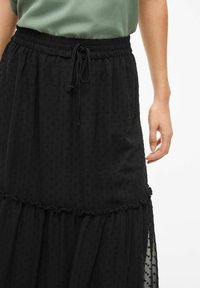 Jupe noire avec un design à volants et un motif texturé à pois. Taille élastique avec cordon de serrage et accents de volants sur les coutures.