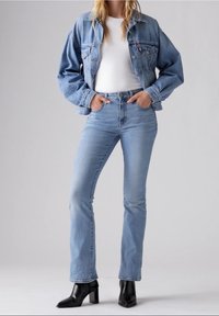 Chaqueta de mezclilla azul claro con un ajuste relajado, combinada con pantalones vaqueros azul claro y botines negros de tacón. Textura suave, diseño casual.