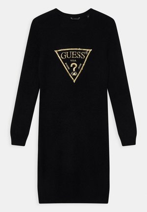 Czarna dzianinowa sukienka z długim rękawem, z trójkątnym logo Guess obramowanym złotem i napisem "GUESS U.S.A. Washed Jeans" umieszczonym centralnie na piersi.
