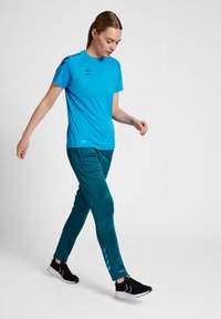 Blauw sportshirt met korte mouwen, gecombineerd met teal joggingsbroek met zijzakken en een patroon van chevrons vlakbij de zoom.