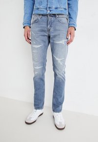 Ljusblå, slitna jeans med flera hål, smal passform och en urtvättad textur, kombinerat med vita sneakers.